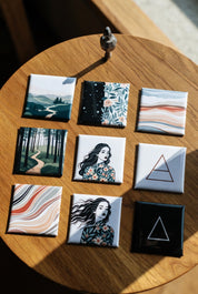 A pack of 9 square custom photo magnets with art prints on a wooden surface