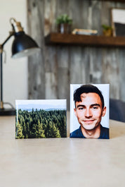 Two 2"x3" magnets on a desk, one with a forest and the other with a person, with a blurred indoor background.