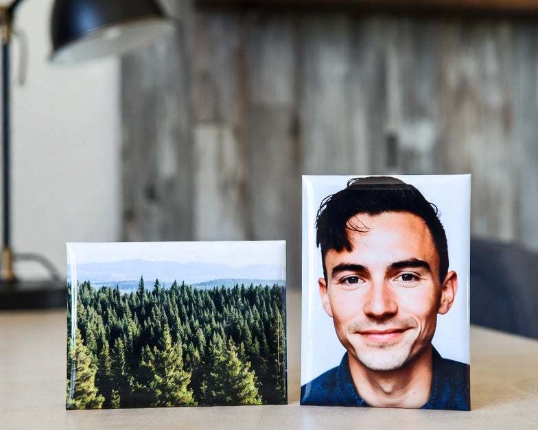 Two 2"x3" magnets on a desk, one with a forest and the other with a person, with a blurred indoor background.