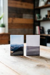 Two 2"x3" magnets of mountain landscapes on a wooden surface.