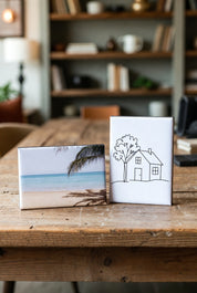 Two custom rectangle photo magnets on a wooden table, one with a beach scene and the other with a house and tree illustration.