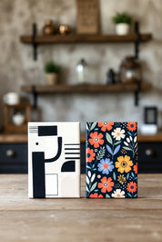 Two 2"x3" magnets with different covers, one with abstract design and the other with floral pattern, on a wooden surface.