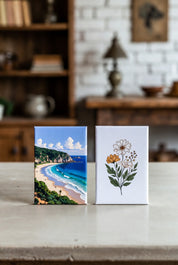 Two 2"x3" custom magnets with scenic and floral designs on a wooden surface.